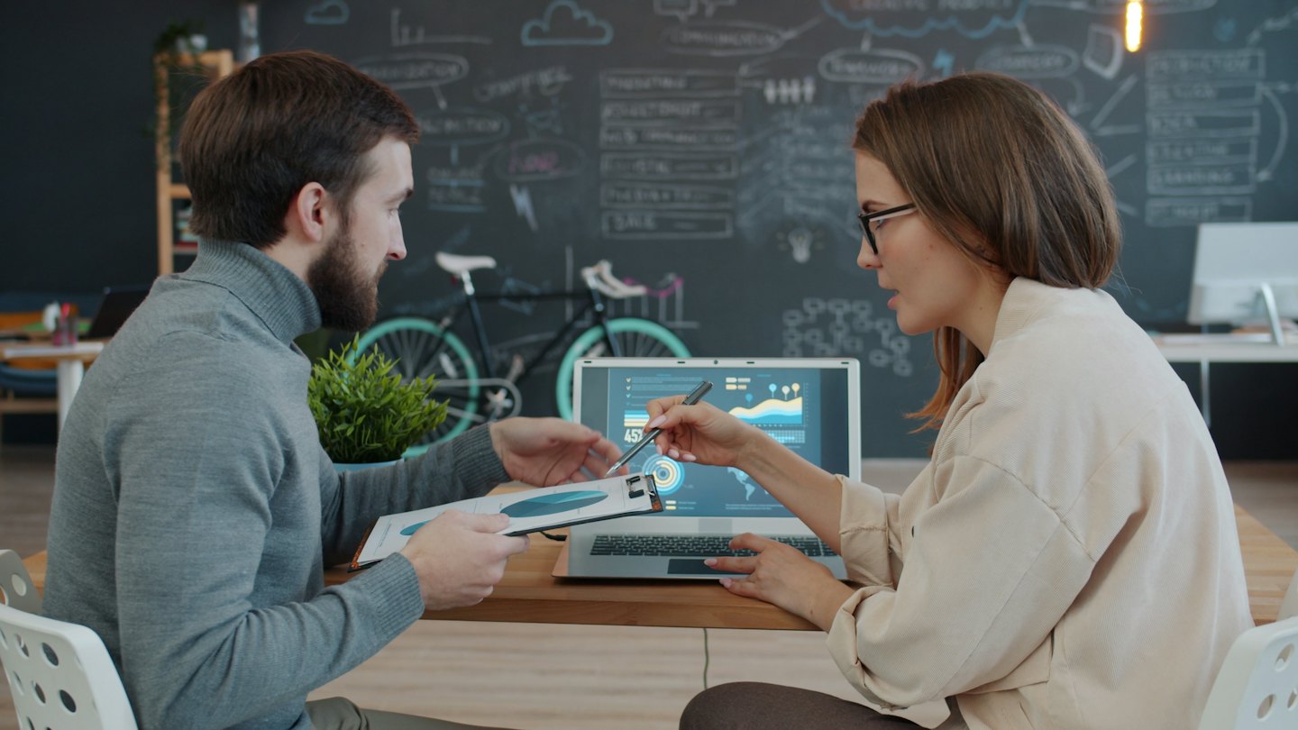 Two businessmen discussing data on a laptop and document.